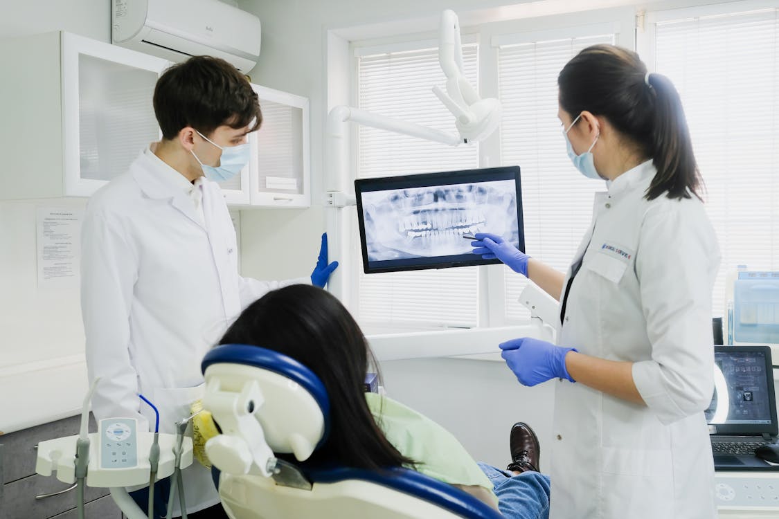 Free Two dentists examine a dental X-ray with a patient in a modern clinic setting. Stock Photo