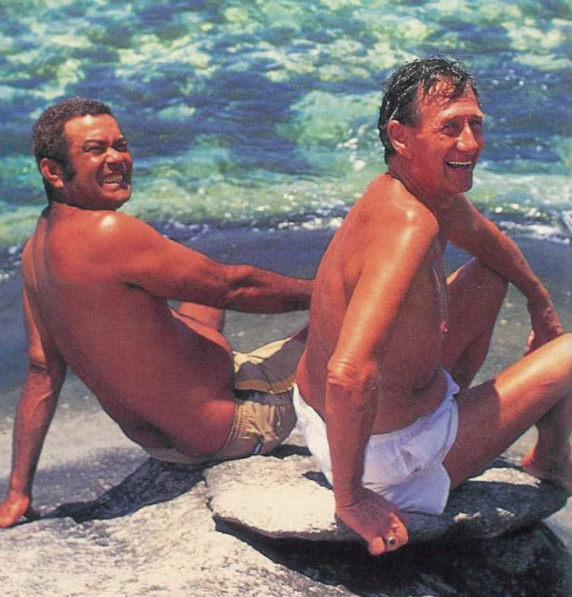 Brendon Grimshaw and René Antoine Lafortune relaxing by crystal-clear tropical waters near Moyenne Island.