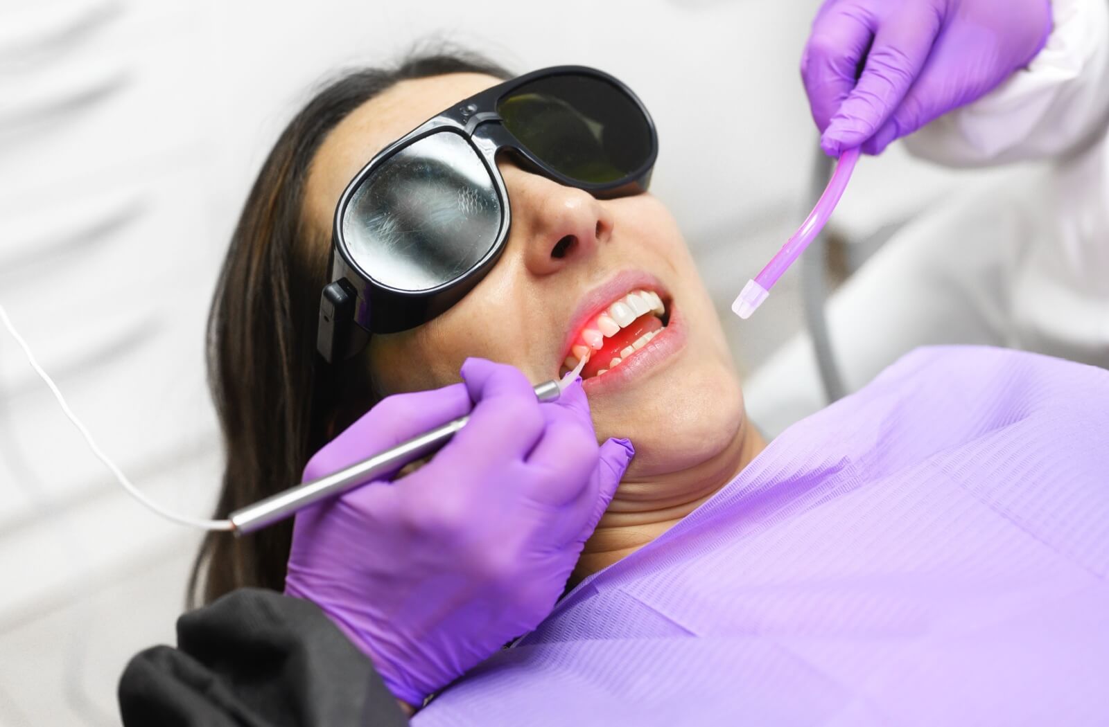 Dentist wearing purple gloves and protective glasses performing laser gum treatment for periodontal disease on a patient