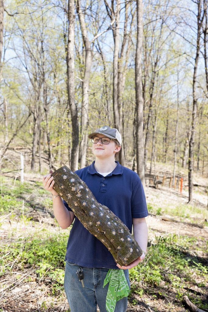 A child holding a log in the woods

AI-generated content may be incorrect.