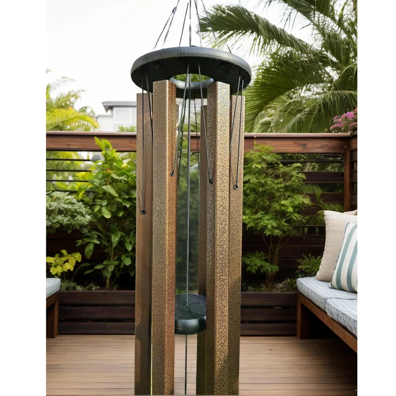 Unique windchimes featuring textured bronze aluminum tubes, black top ring, and deep resonating design, displayed on wooden deck with tropical garden backdrop for outdoor meditation and sound healing