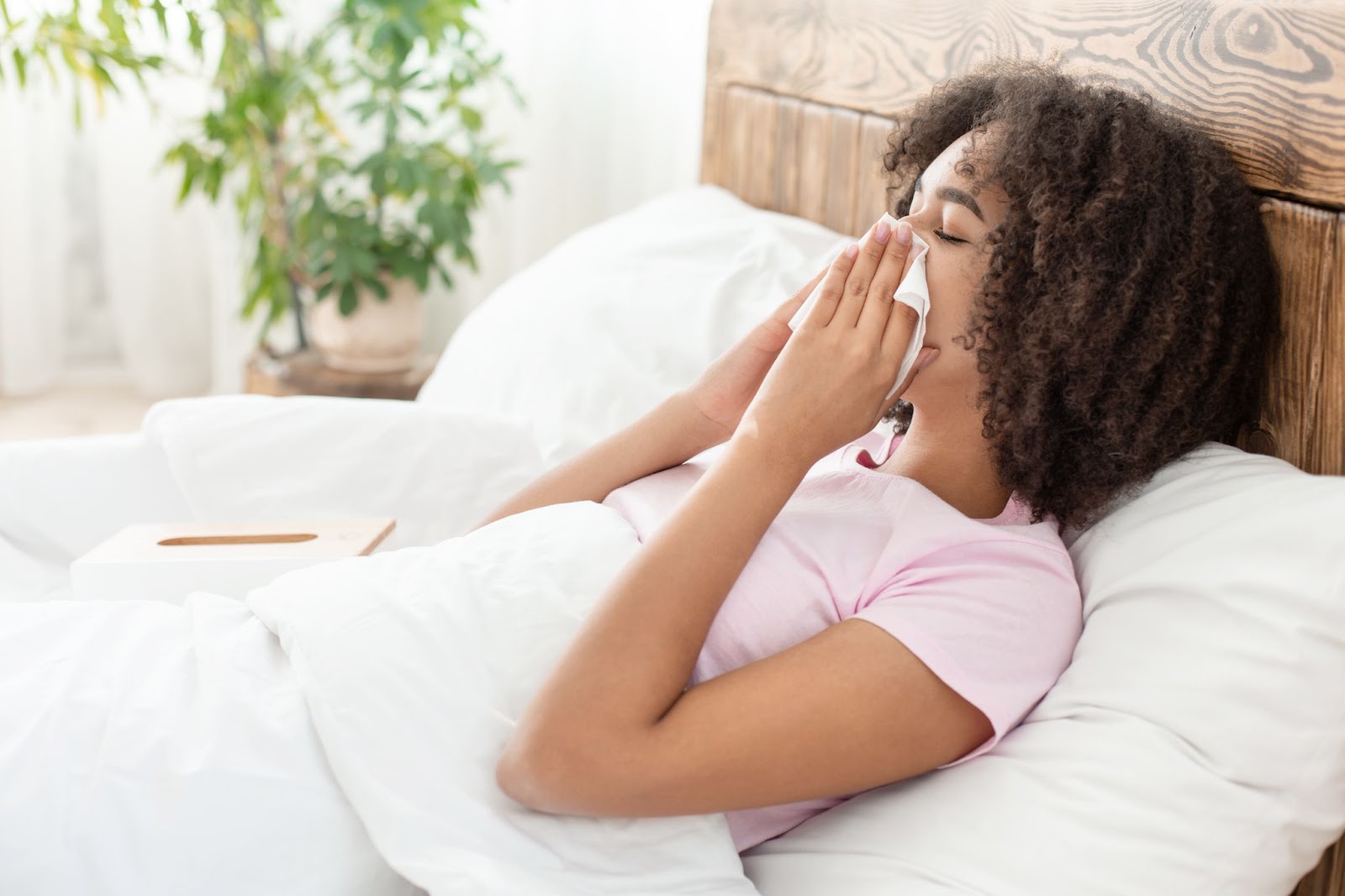 A woman sneezing in bed, illustrating the hypoallergenic benefits of latex foam vs memory foam for allergy sufferers.