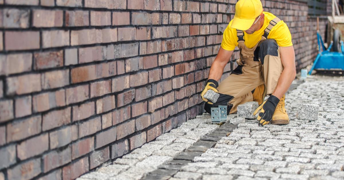 A person in yellow uniform and yellow hat placing bricks on a brick wall

Description automatically generated