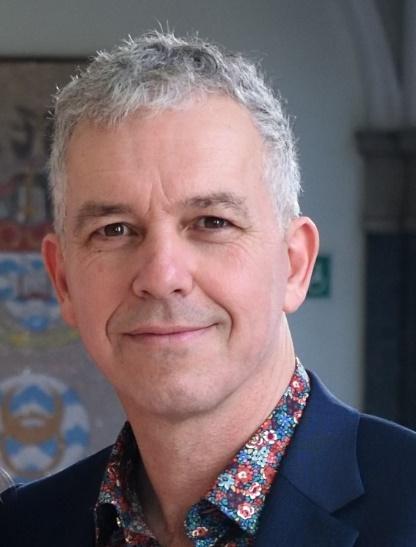 A person with grey hair wearing a floral shirt

Description automatically generated