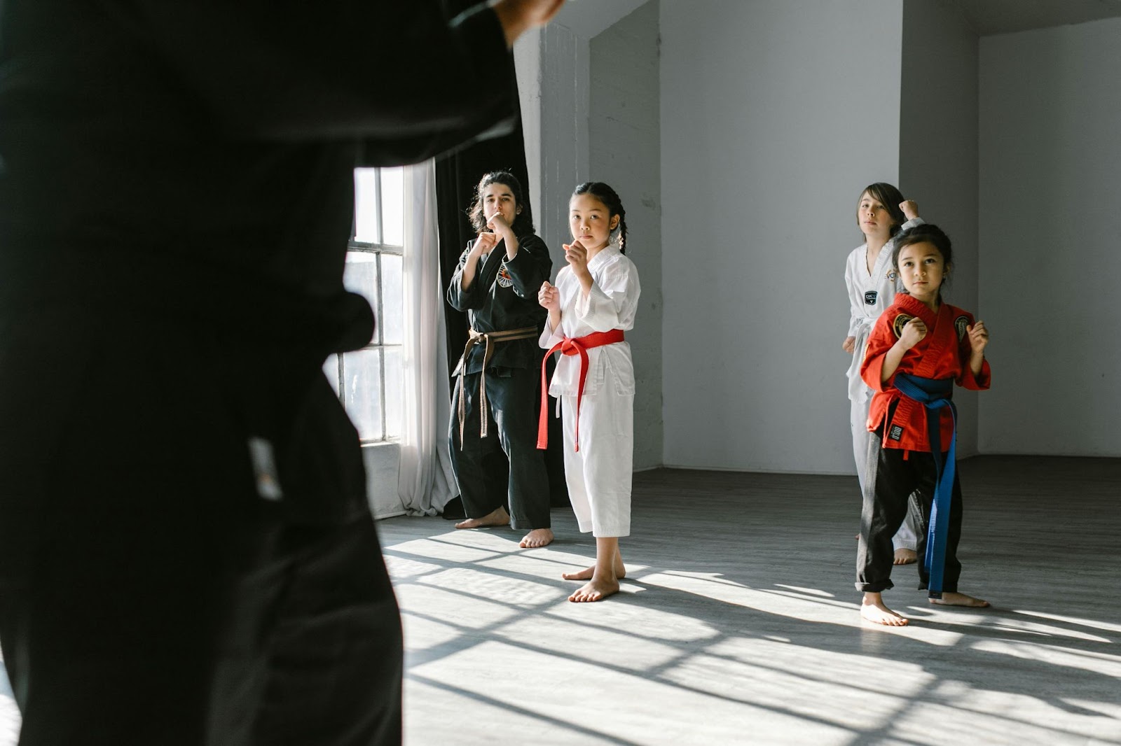 Four children in martial arts uniforms standing in a ready stance in front of their instructor in a room 