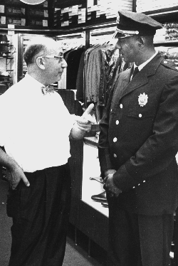 Lloyd Sealy is in his uniform, speaking to a man in a store.