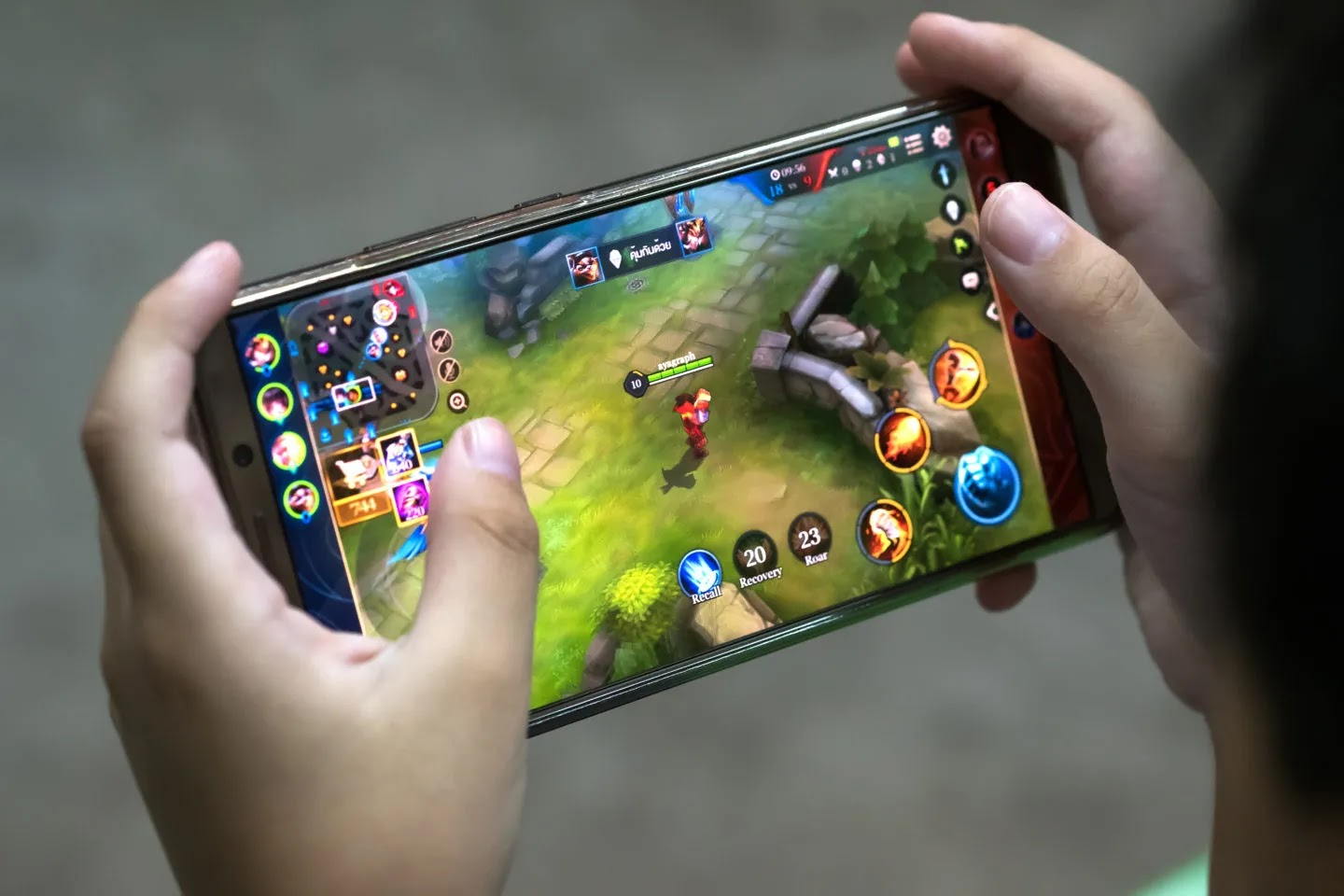 Mãos seguram celular, com interface de game mobile aberta.