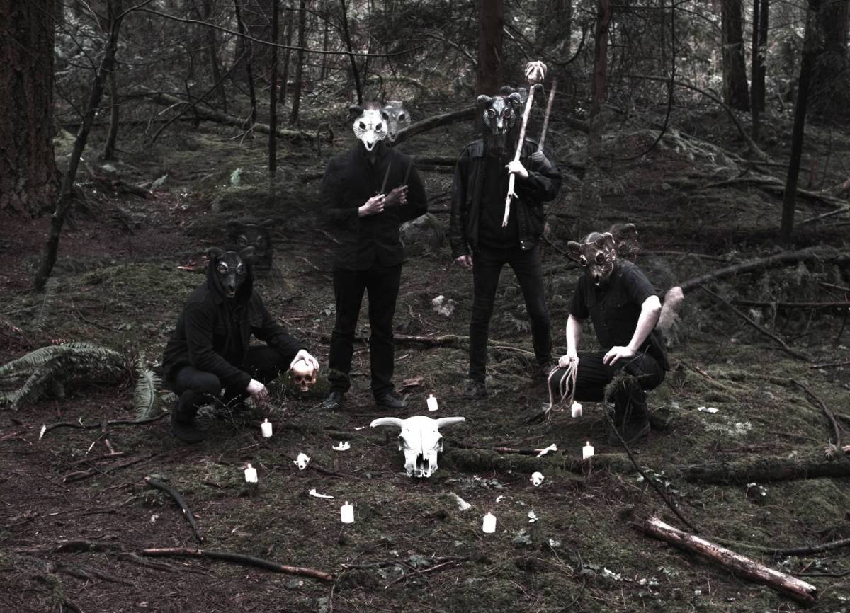 A desaturated photo of four people wearing animal masks in the foods, around a goat skull