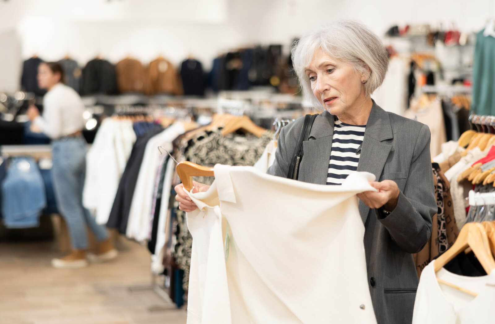 An older adult shopping in front of racks of clothes examining a comfortable white shirt.
