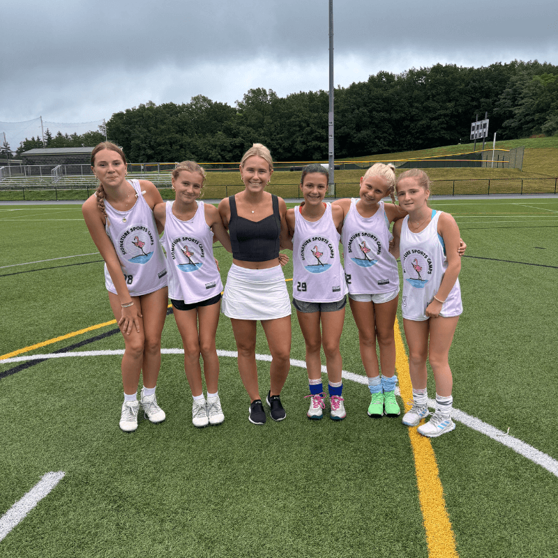 Coach at overnight sports camp poses for a photo on the field with a group of girls