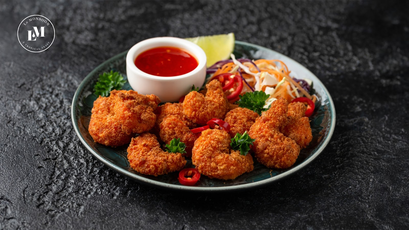 Crunchy golden fried prawns with a spicy dipping sauce on a dark plate.