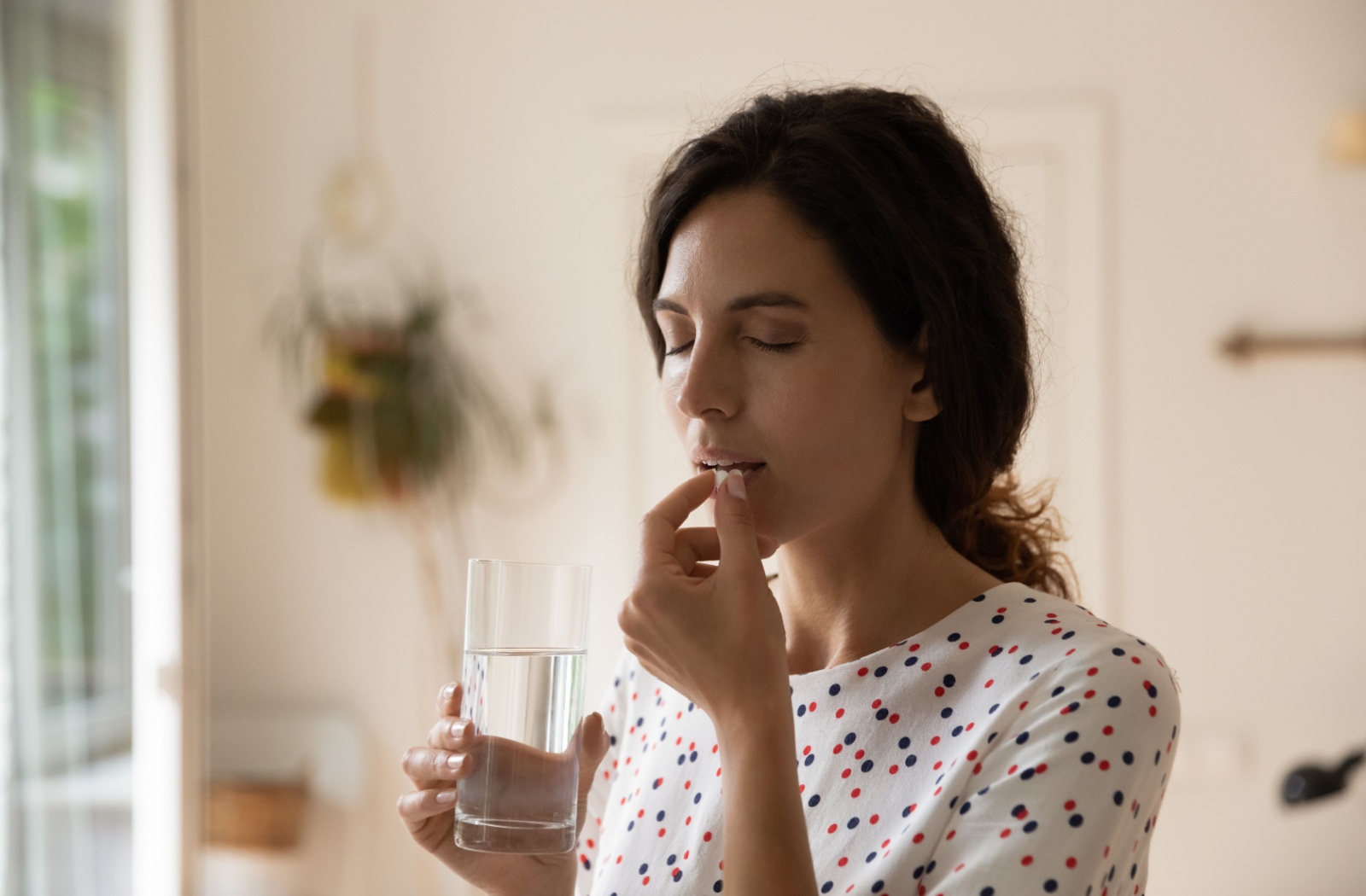 Person at home taking a pain reliever pill with a glass of water, appearing calm and focused.