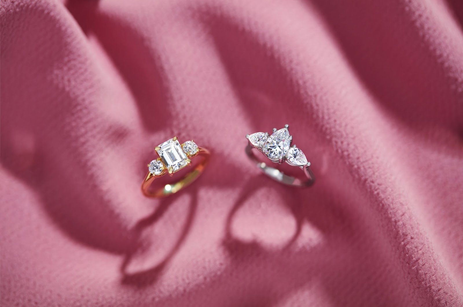 Two three-stone engagement rings. One is in yellow gold and the other is in white gold.