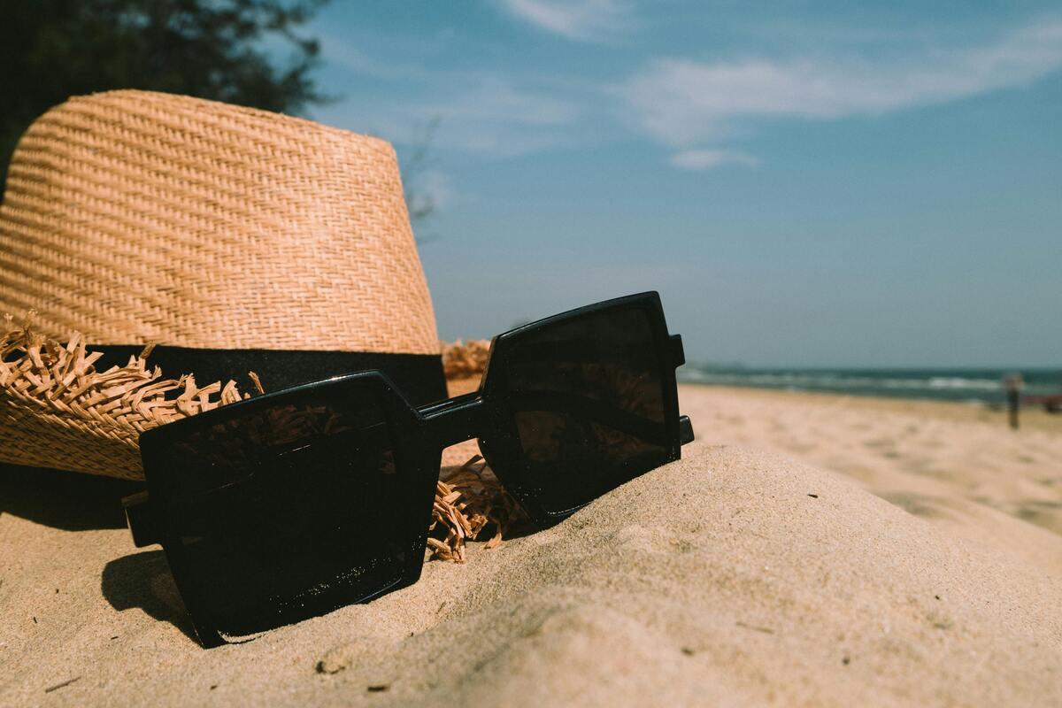 A hat and sunglasses placed on the beach sand 
