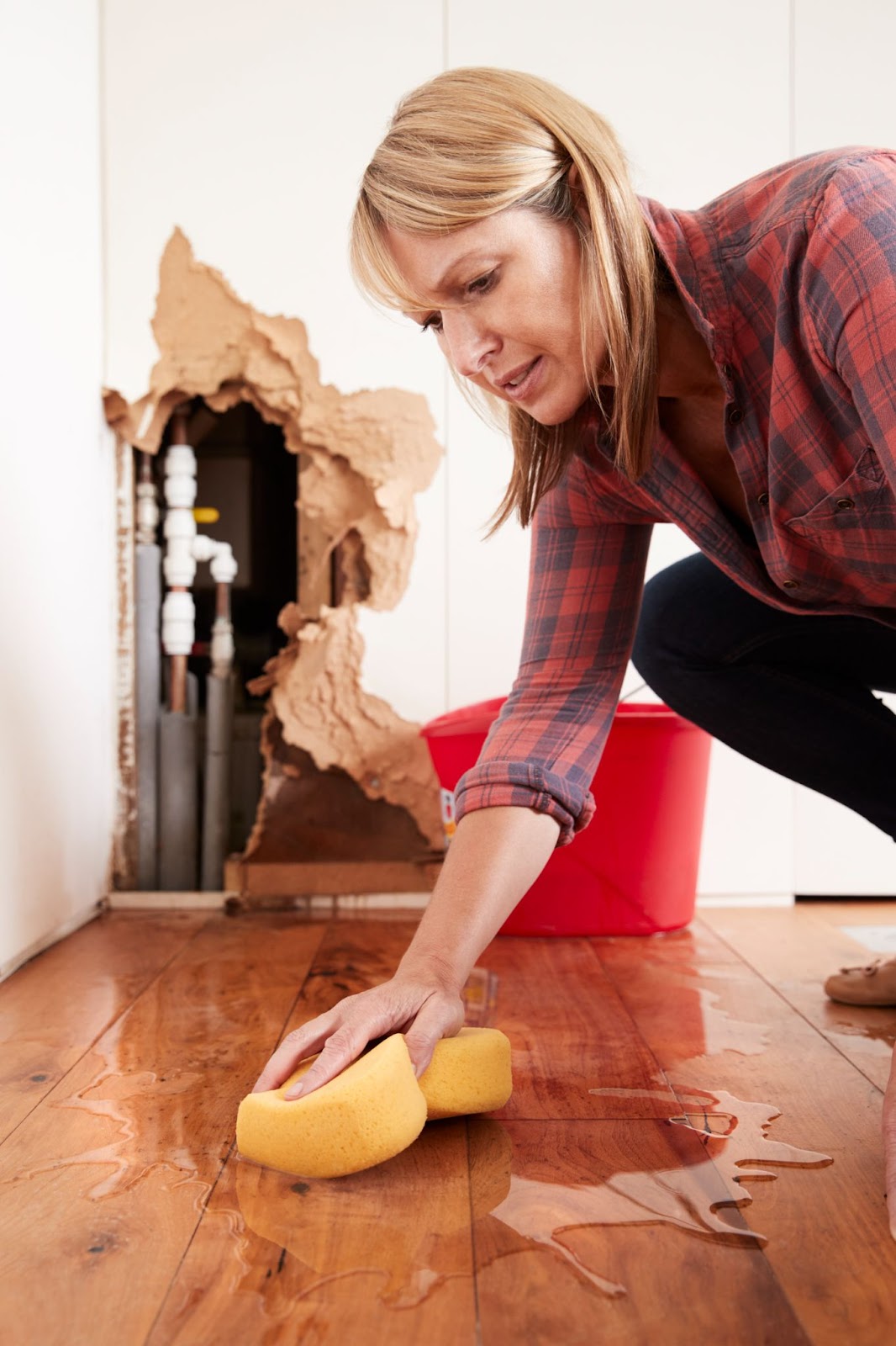 A woman mops up water from a burst pipe under the sink with a sponge.