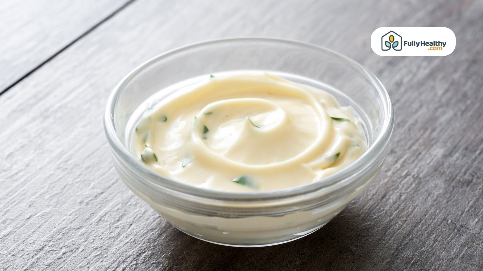 Glass bowl filled with creamy mayonnaise garnished with green herbs