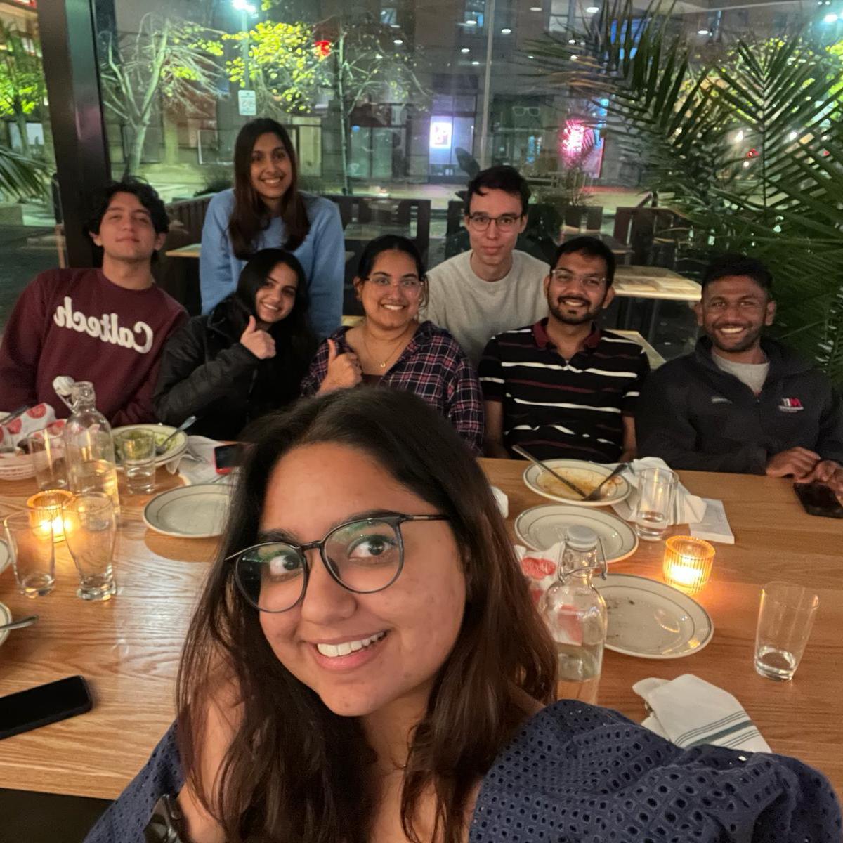 Sanya takes a selfie of herself and a group of friends, all smiling as they sit at a restaurant table.