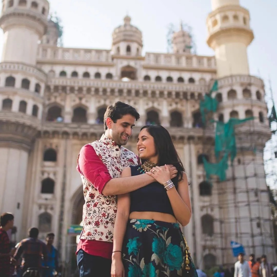 Charming pre-wedding photography of a couple sitting on stairs, with Shilparamam in the background