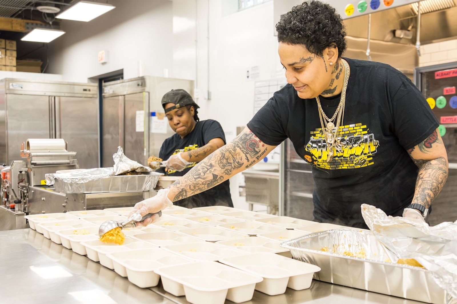 Two food workers filling out trays in a commercial kitchen