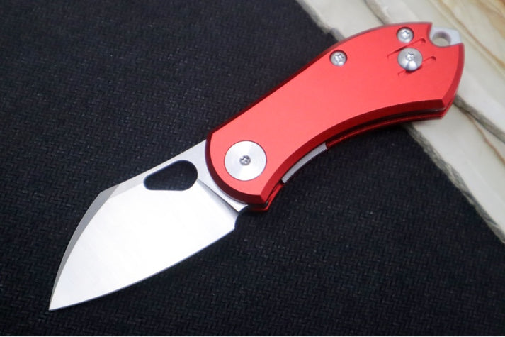 An image showing the GiantMouse Nibbler folder on a solid black and wood background. The knife has a red aluminum handle and a Wharncliffe N690 blade.