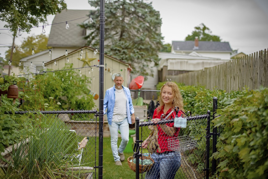 A couple exiting a garden through a gated fence. 