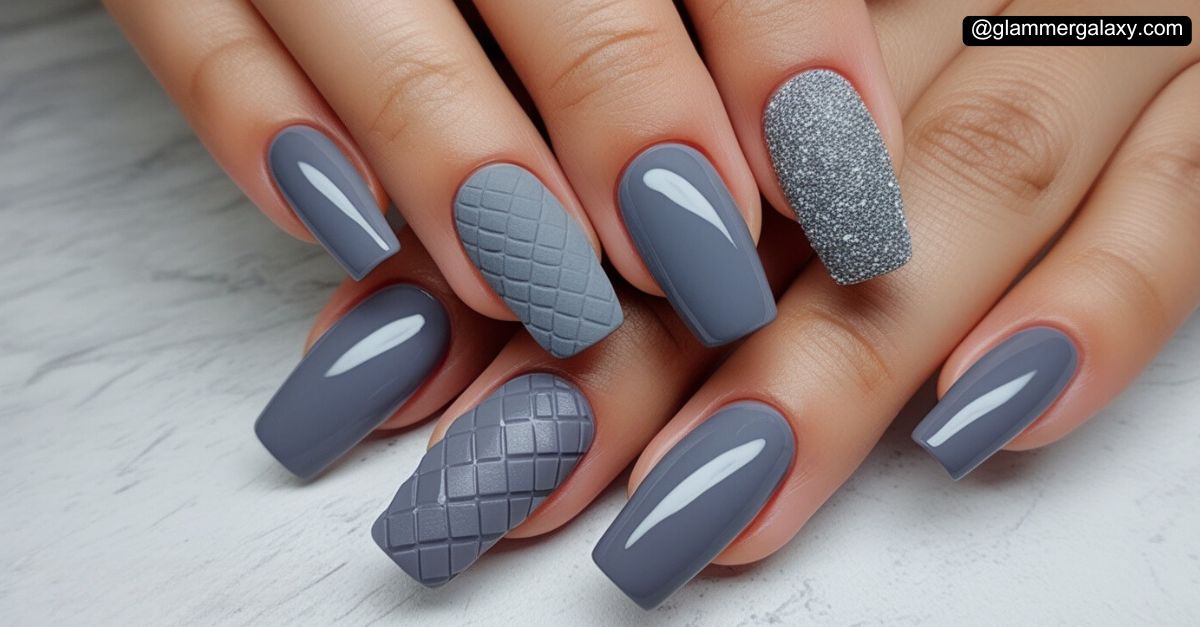 Manicured nails with grey polish and textured accent designs.