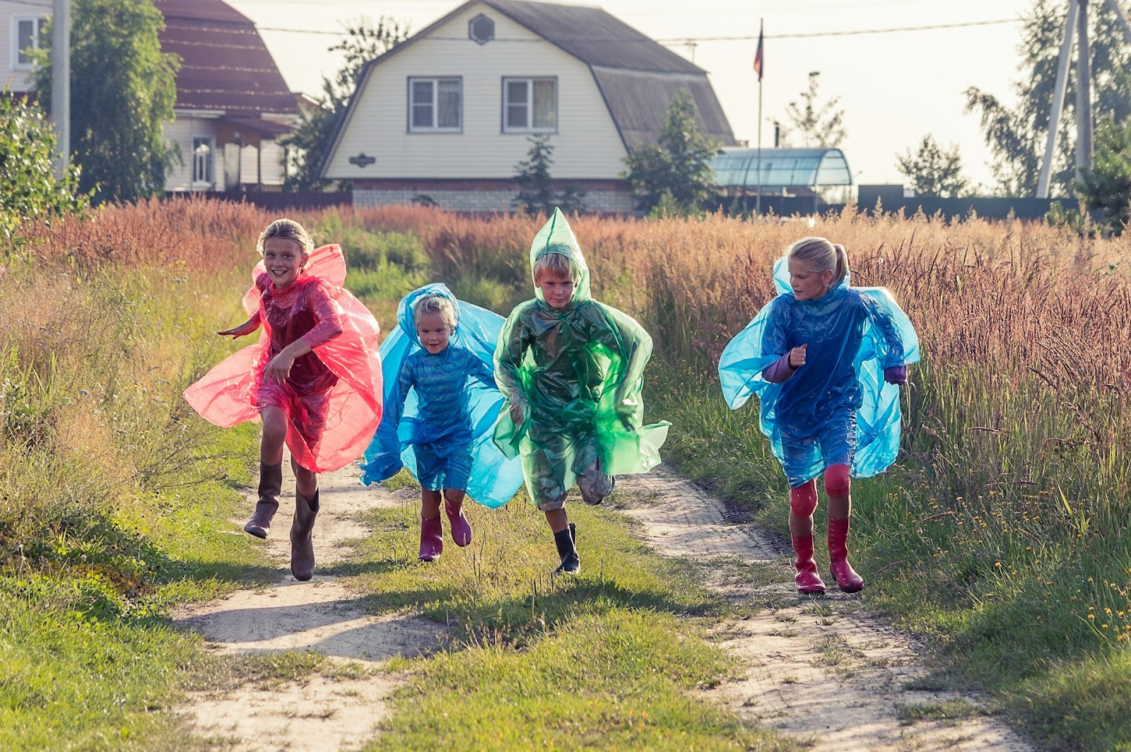 Four children dressed in colorful capes run joyfully down a dirt path.