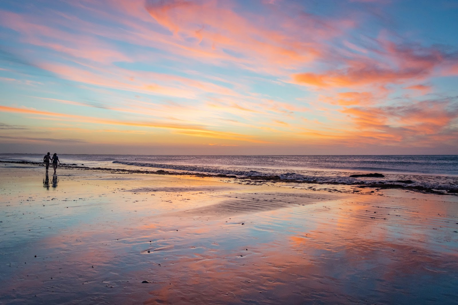 Golden sand at Jericoacoara beach with a stunning sunset over the ocean and a couple enjoying the view.