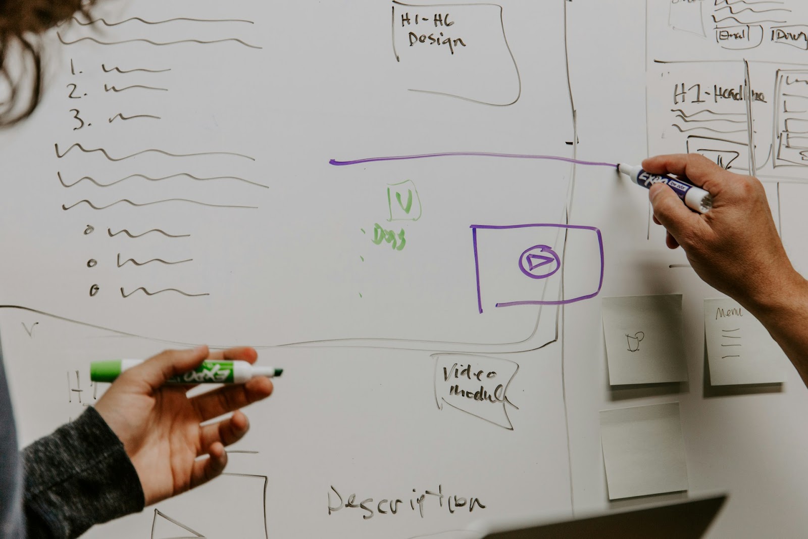 Two individuals collaborating and writing ideas on a whiteboard in a bright, open workspace.