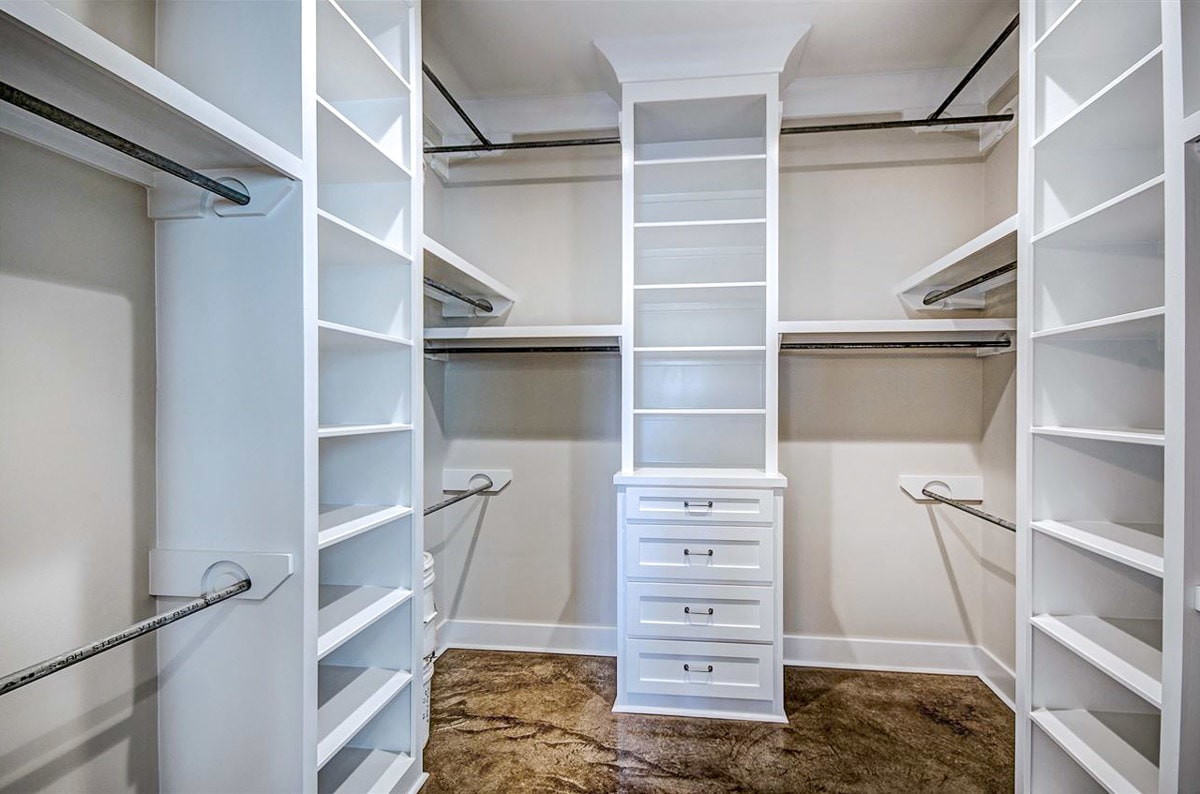 Walk-in closet with white built-in shelves and pole racks.