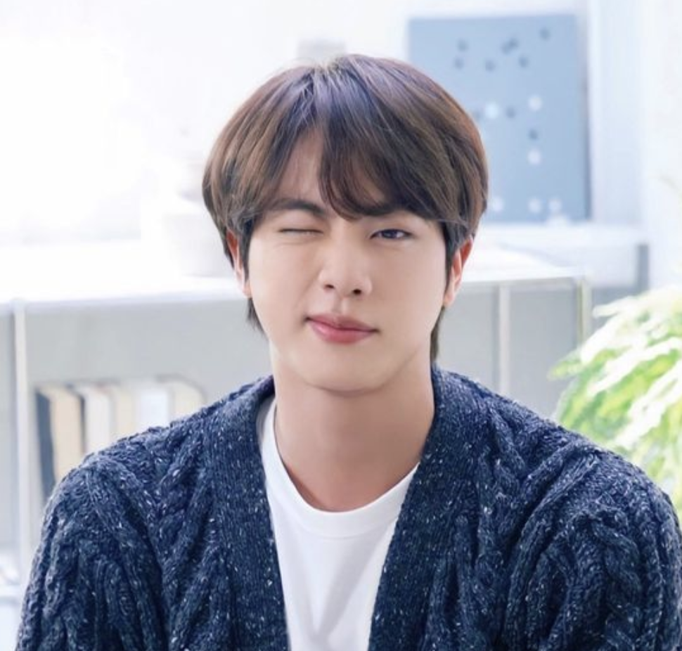 A picture of BST Jin wearing a navy blue sweater and a white vest winking his left eye