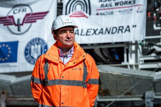 A person in an orange jacket and white hard hat  Description automatically generated