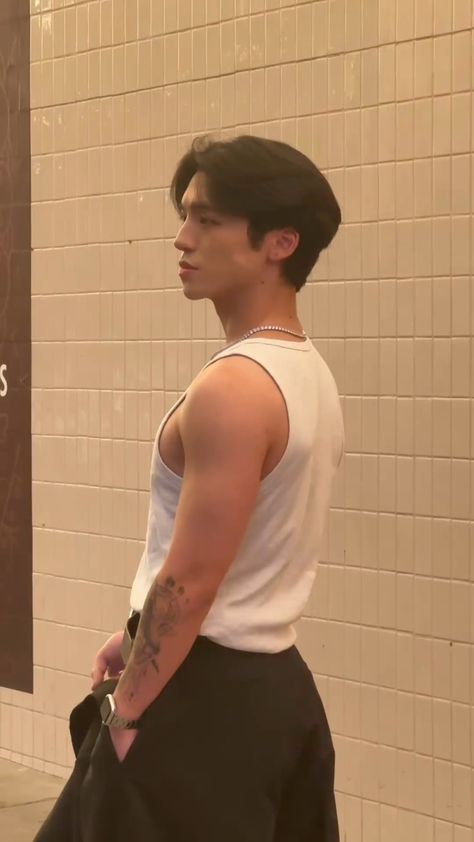 This  contain an image of Beomhan with tattoos standing in front of a wall holding a black bag and wearing a white tank top