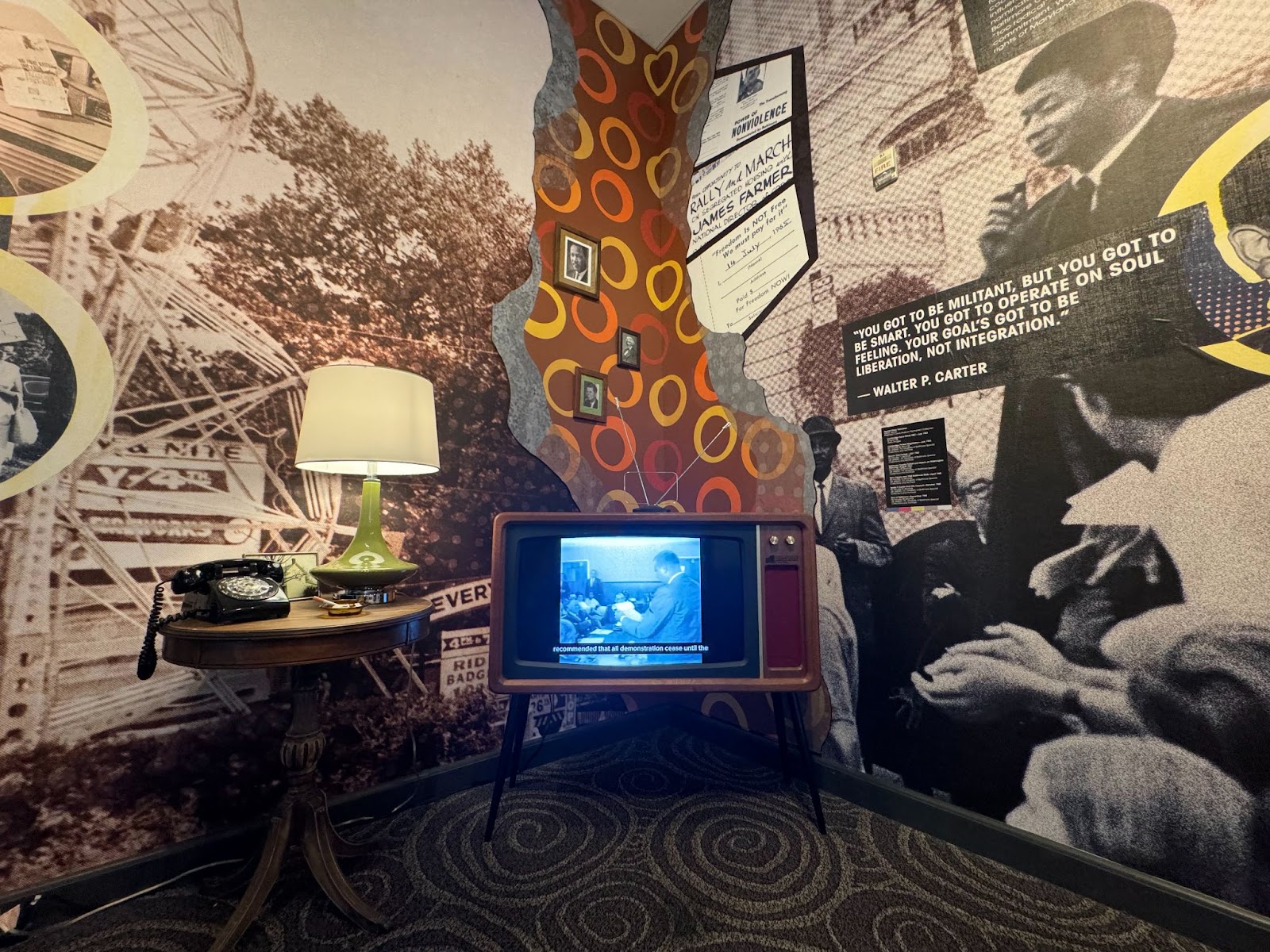 A living room display with an outdated phone, lamp, and television and old photographs as wallpaper.