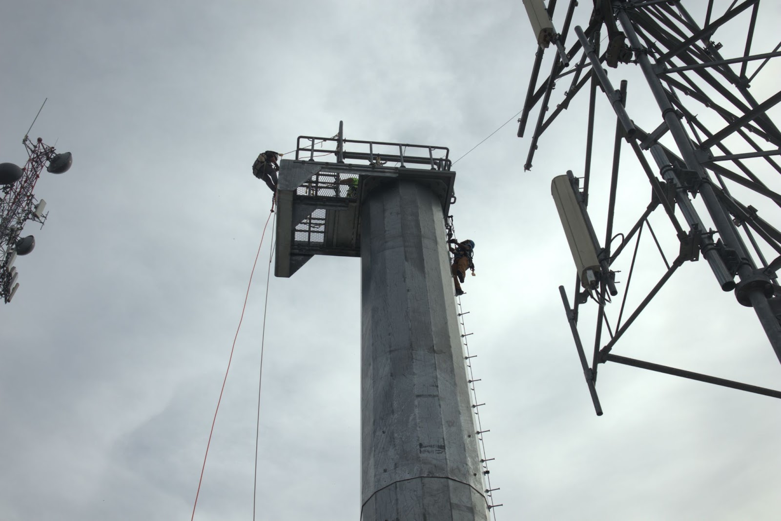 Pinnacle Career Institute outdoor climbing lab we see a telecommunications tower with a student on it against a gray sky