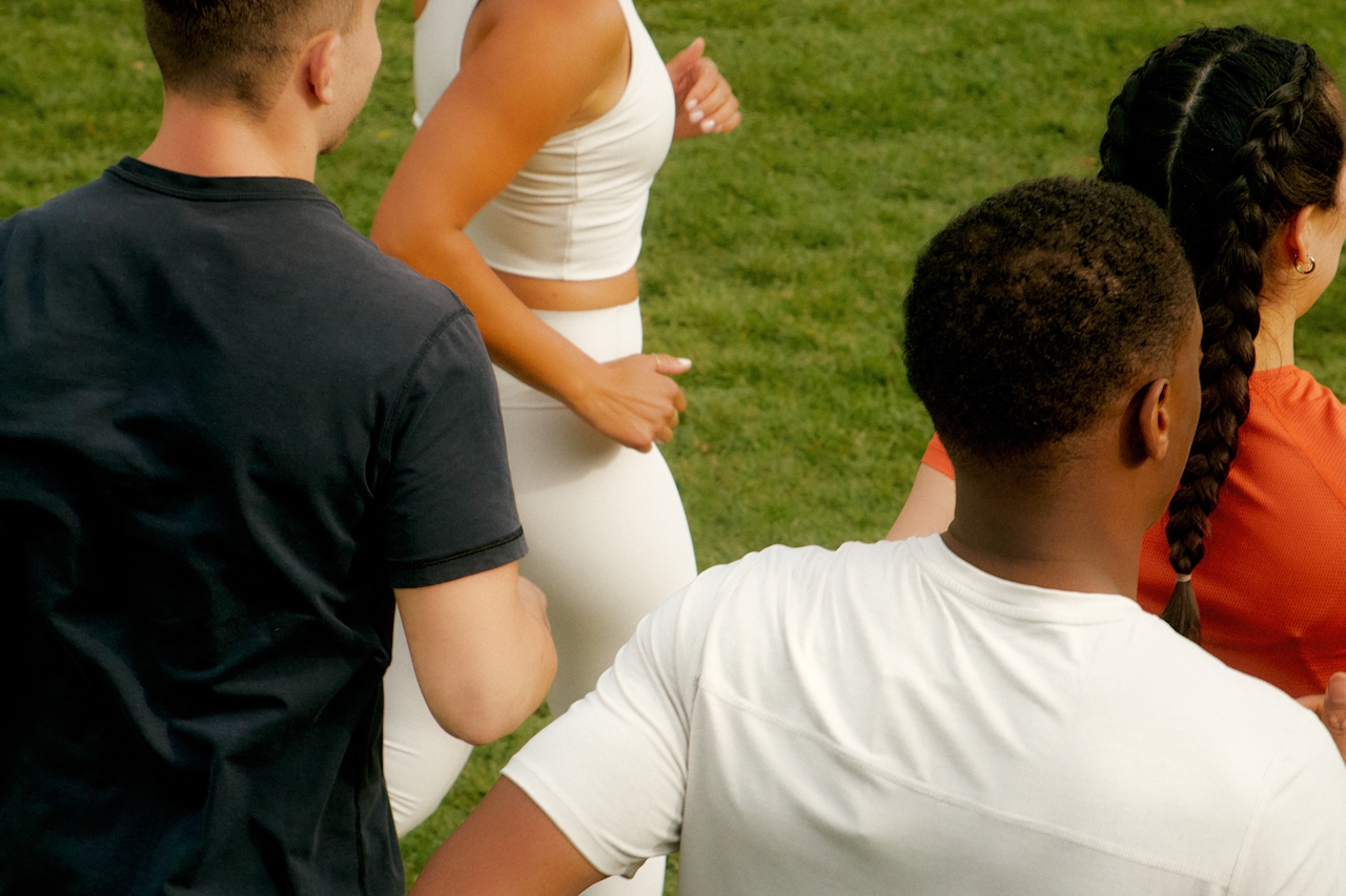 Group of adults jogging together outdoors on a grassy field, wearing athletic activewear during a fitness warm-up session.