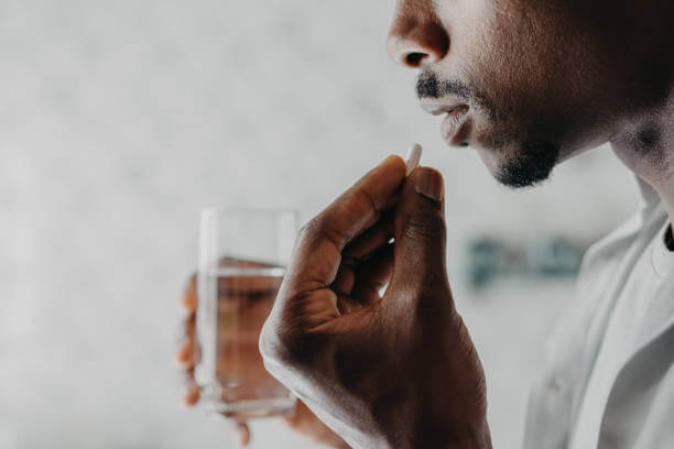 A man holding a glass of water while taking a multivitamin pill, emphasizing daily health and wellness.