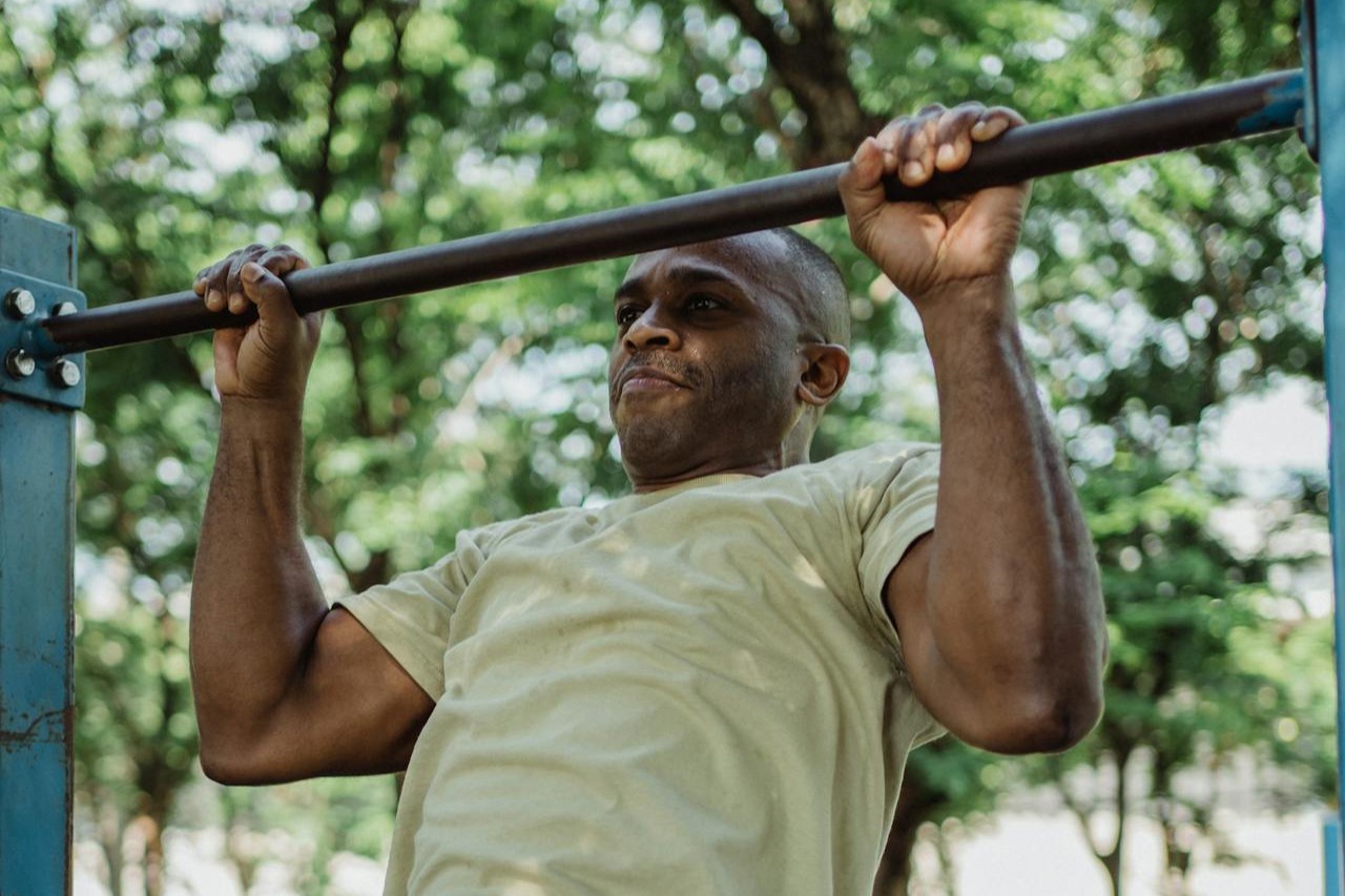 A man performing a pull-up outdoors on a metal bar.