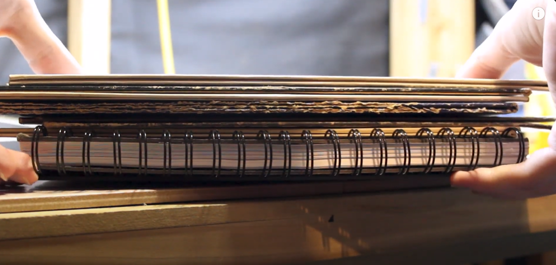 Stack of vinyl records placed between cardboard sheets and a spiral-bound notebook. 