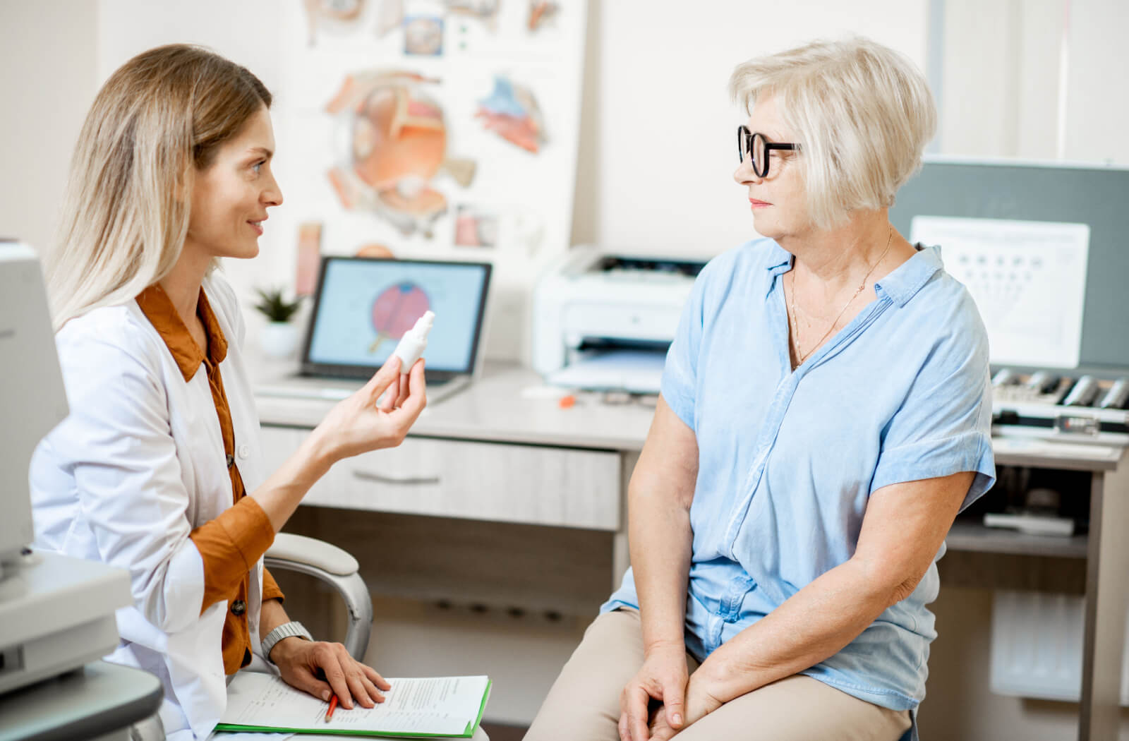 An optometrist holding up a bottle of eye drops explaining to a middle-aged patient the difference between myopia, hyperopia, and presbyopia.