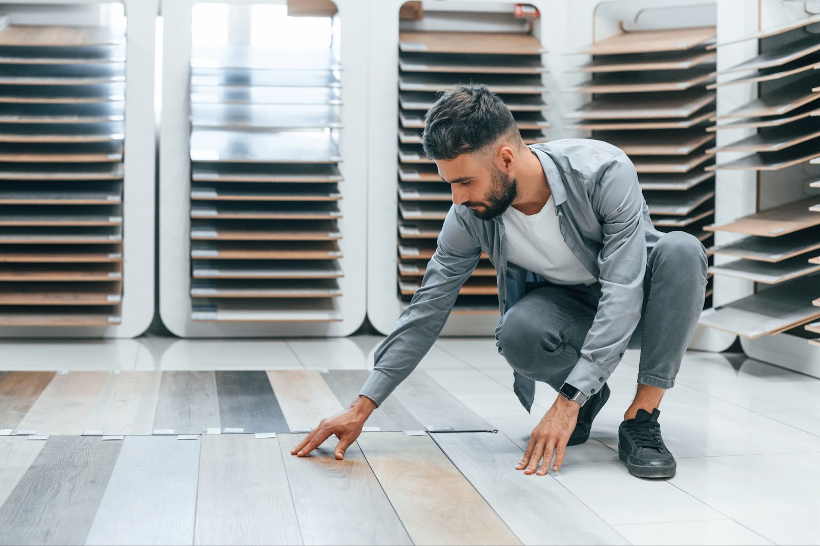 A man carefully examines and selects flooring materials from various wood-like samples displayed in a showroom.