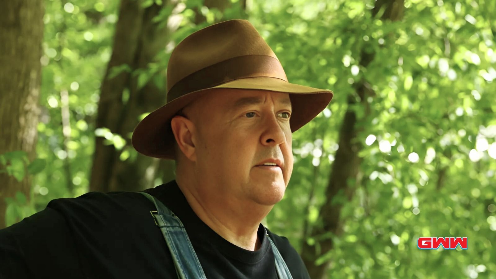 Mark Ramsey in overalls and hat, standing in a wooded area.