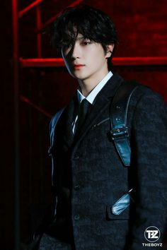 This contain an image of kim hyunjae  wearing a suit and tie in front of a red light with his hand on his hip