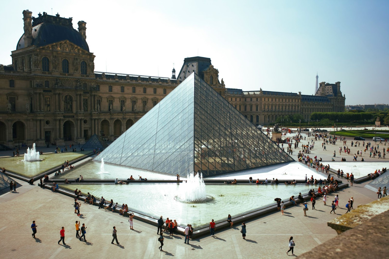 People walking past the famous Louvre Pyramid. This iconic glass and metal structure is the entrance to the Louvre Museum in Paris