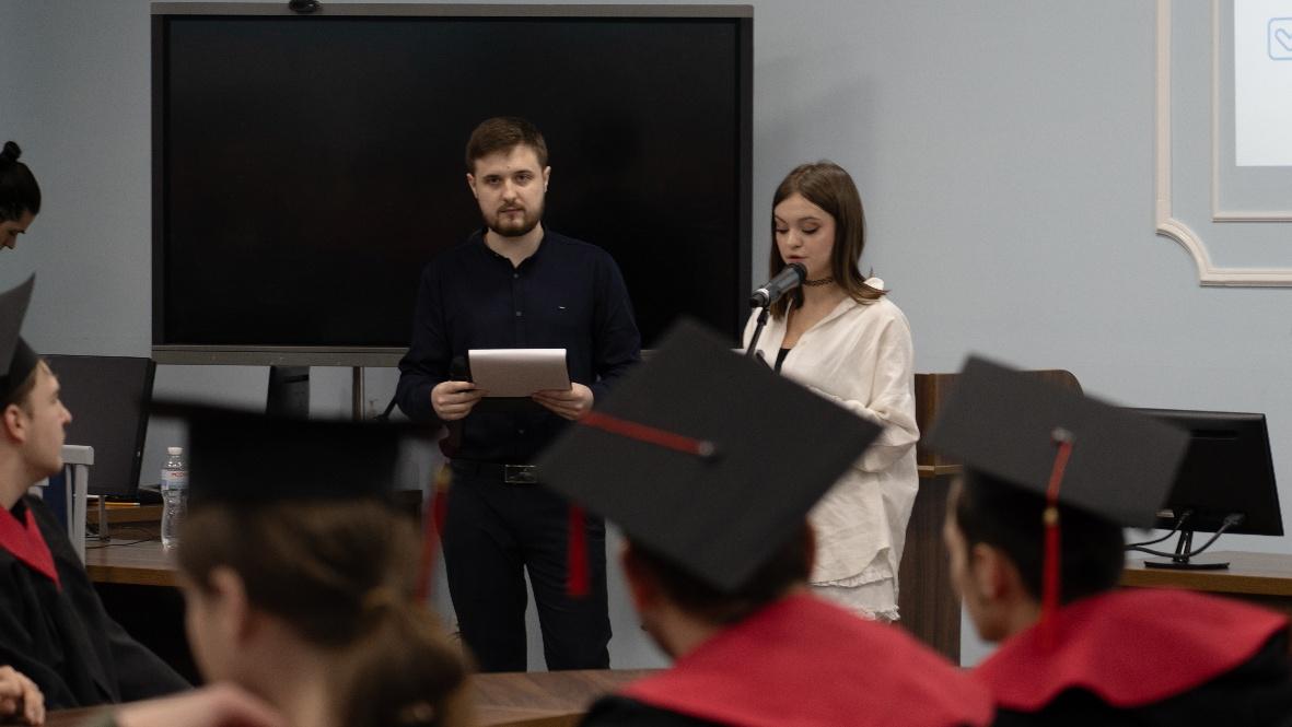 A person and person standing in front of a black screenDescription automatically generated