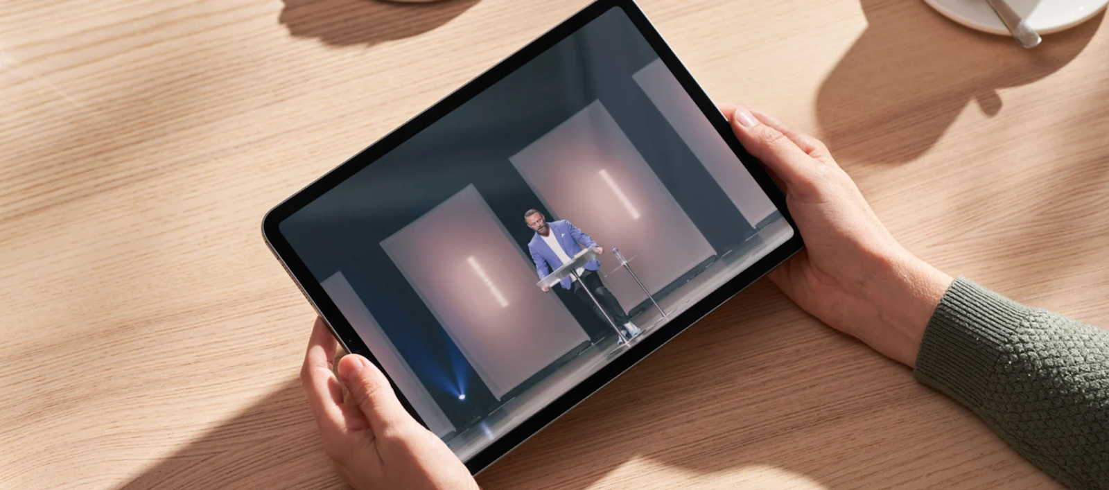A woman's hands holding a tablet at a table watching a live video stream