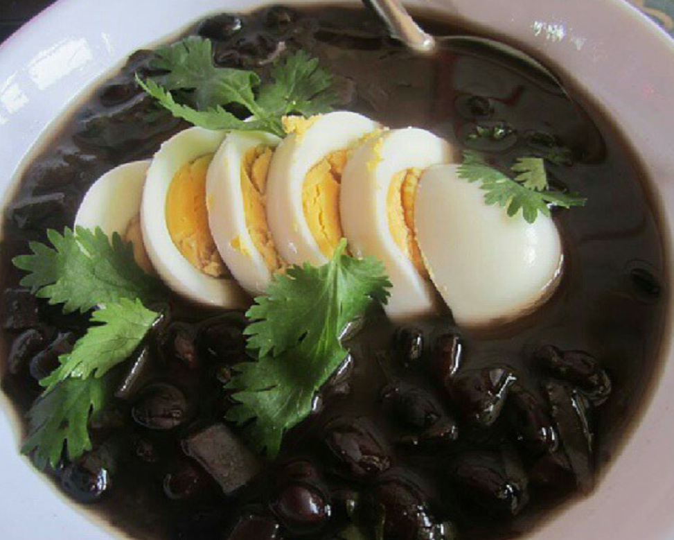 Bowl of Sopa Negra with eggs and cilantro garnish.