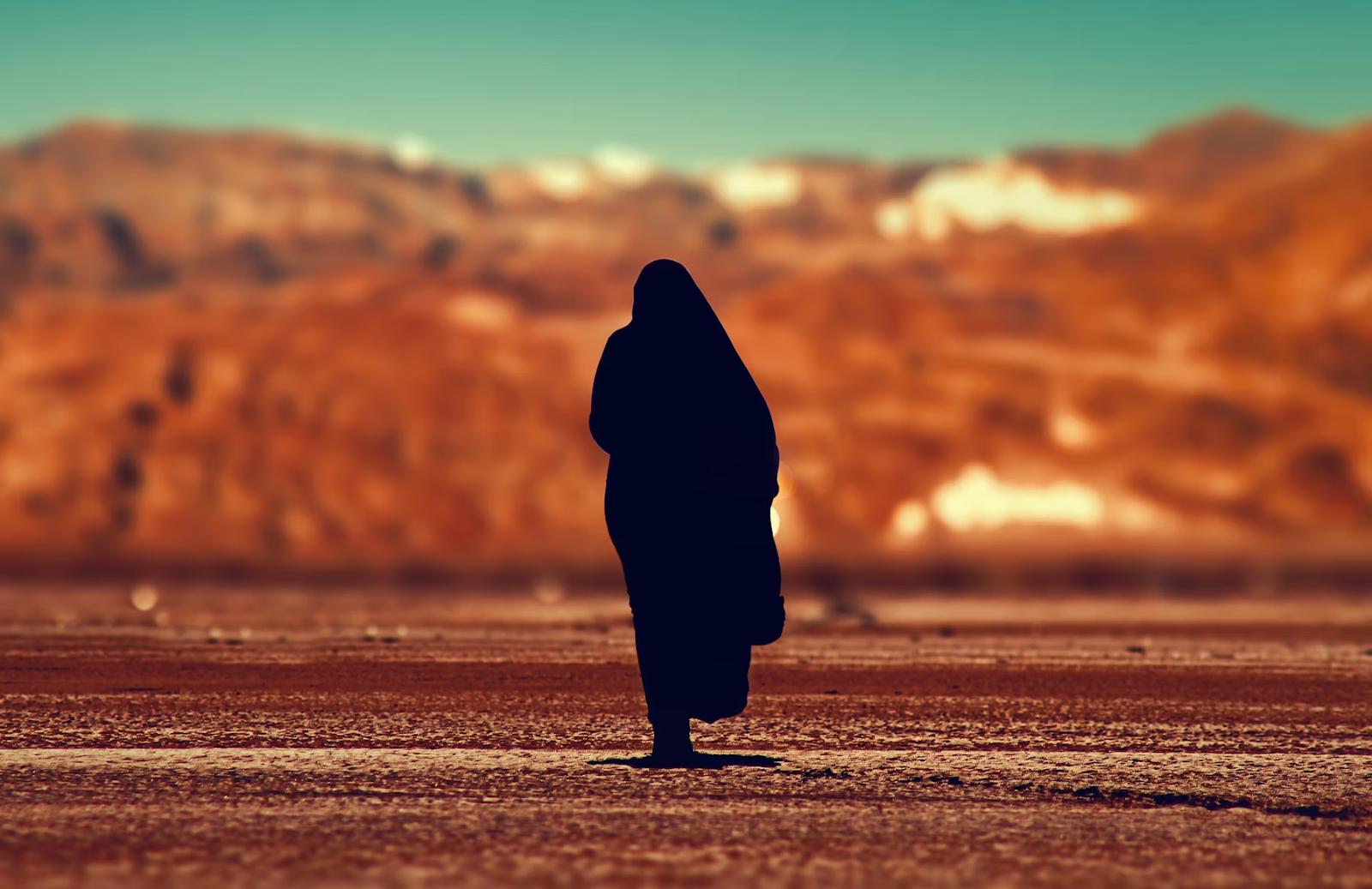 A woman in a desert wearing a black Abaya in Saudi Arabia - (Credits Unsplash)