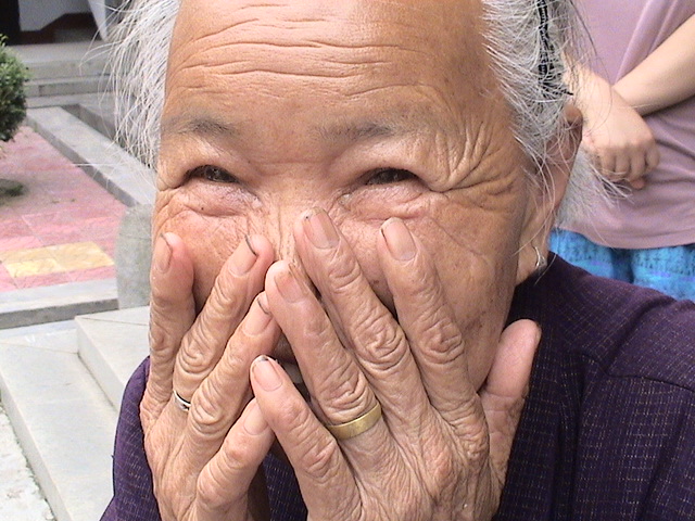 Image:  Asian woman laughing with her hands over her mouth.