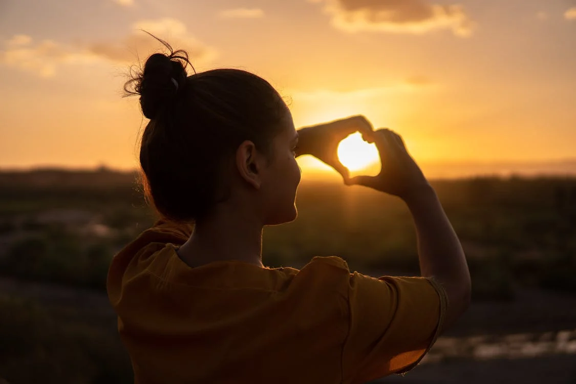 A woman making the shape of a heart next to the sun